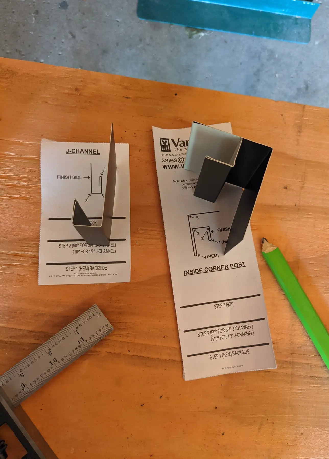 Printed J-channel and inside-corner diagrams beside folded aluminum samples, ruler, and pencil.