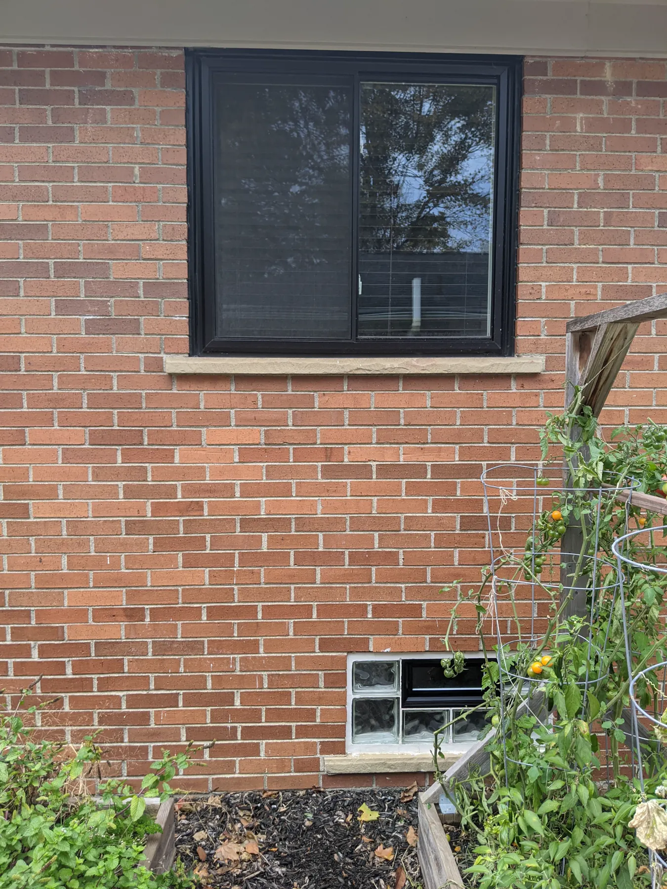 Brick wall with a large black window above and a freshly painted black vent in the glass-block opening below.