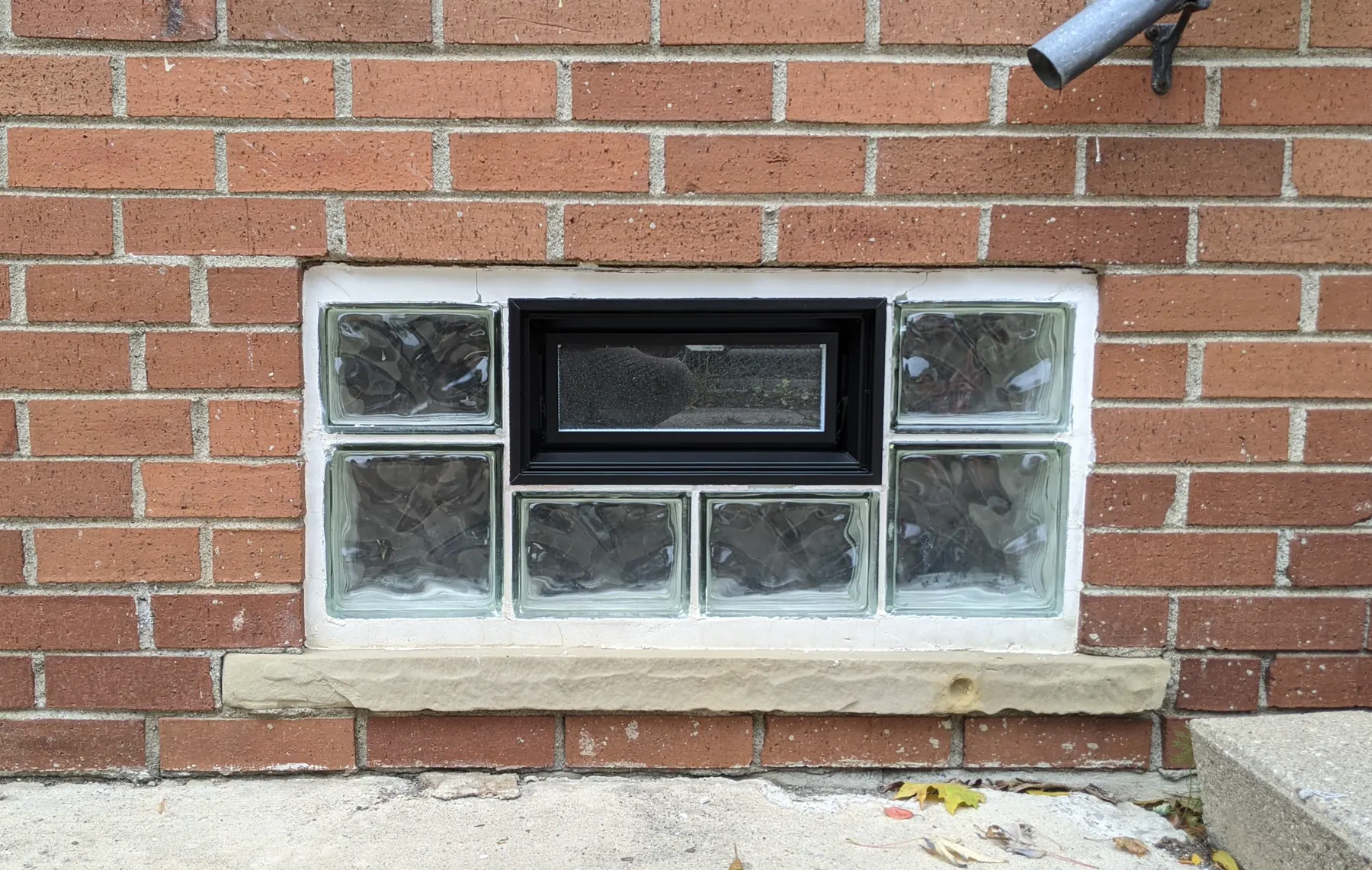 Close view of a black operable vent centered among glass blocks after the masking was removed.