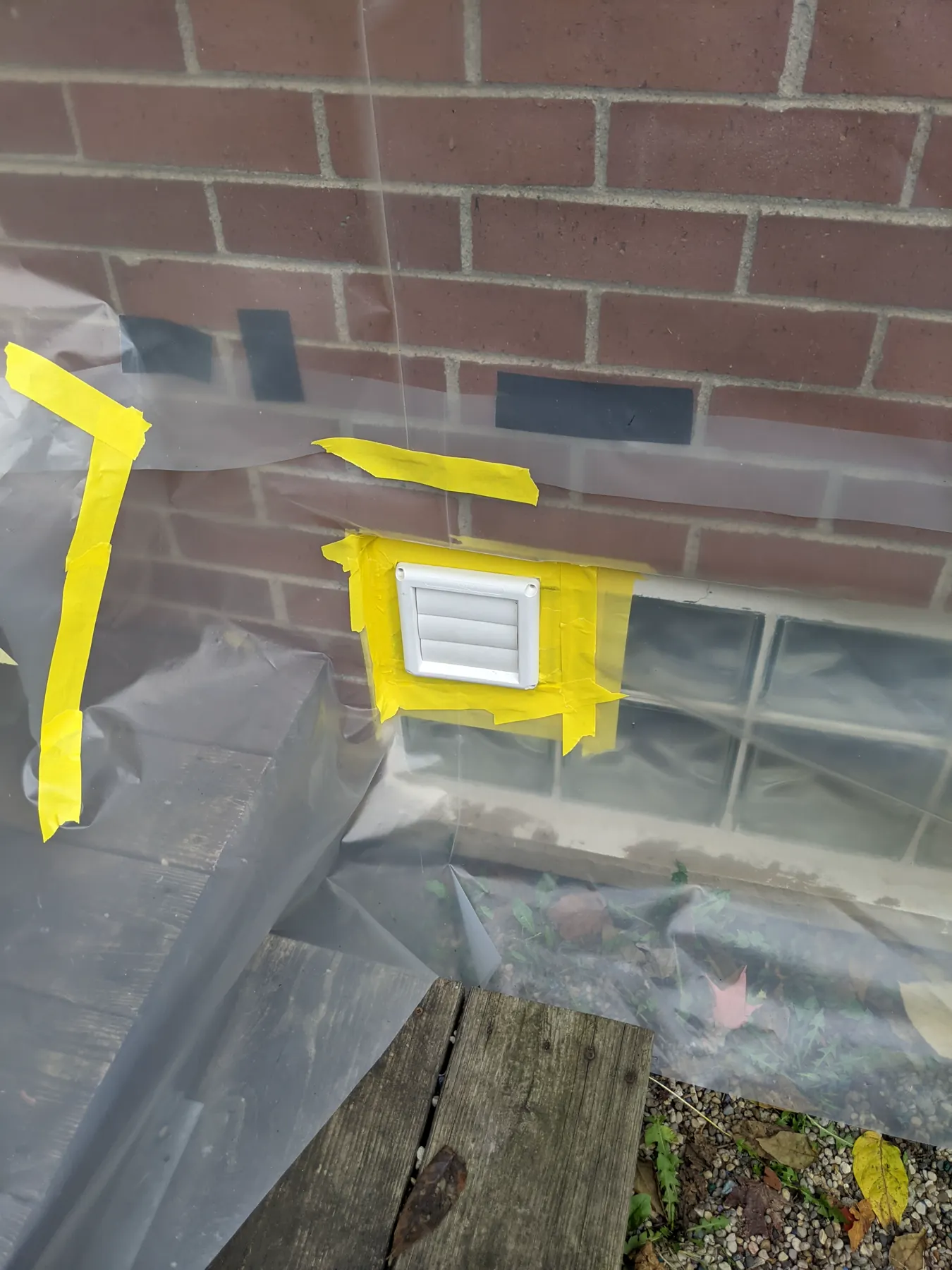 White louvered vent masked in place with tape and plastic protecting the adjacent glass blocks and deck.