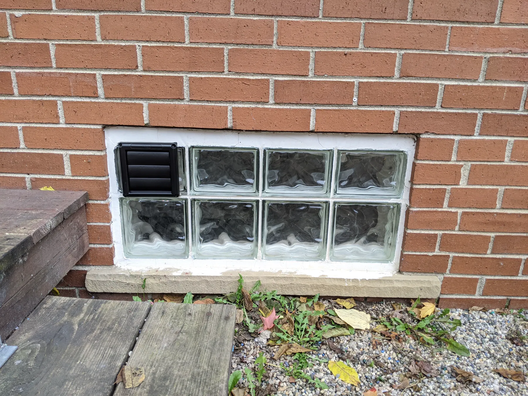 Small louvered vent installed in black within a glass-block basement window.