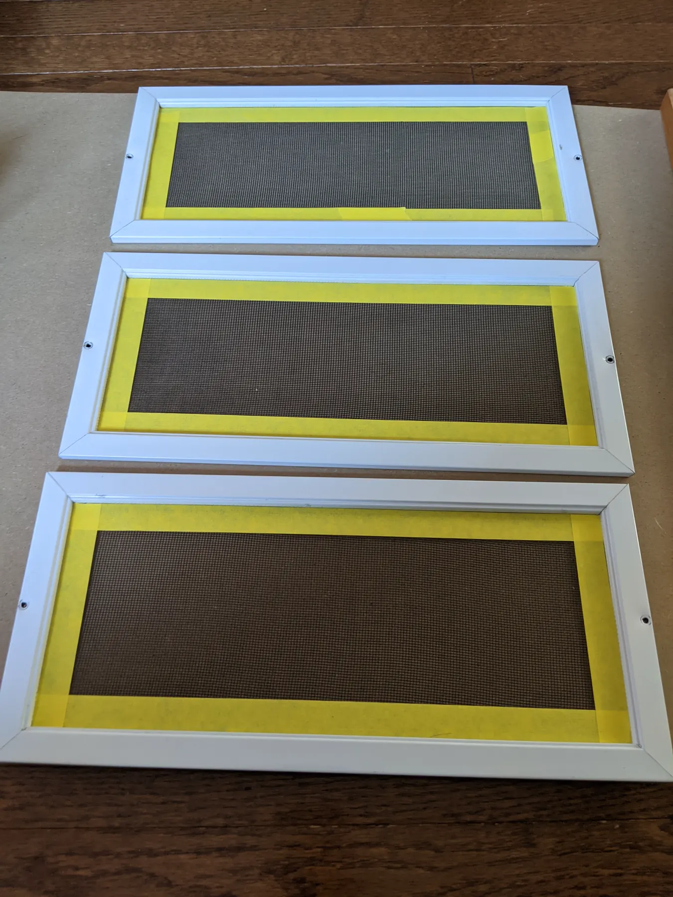 Three white removable screen inserts with their mesh carefully masked in yellow tape.