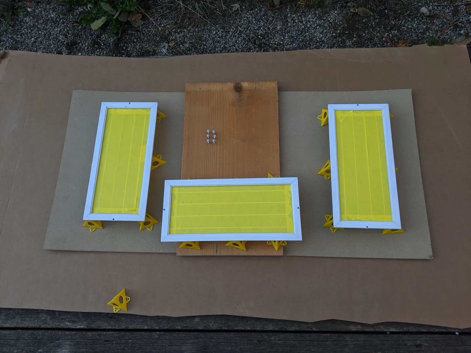 Three white vent frames with their centers masked, raised on small painting supports beside their screws.