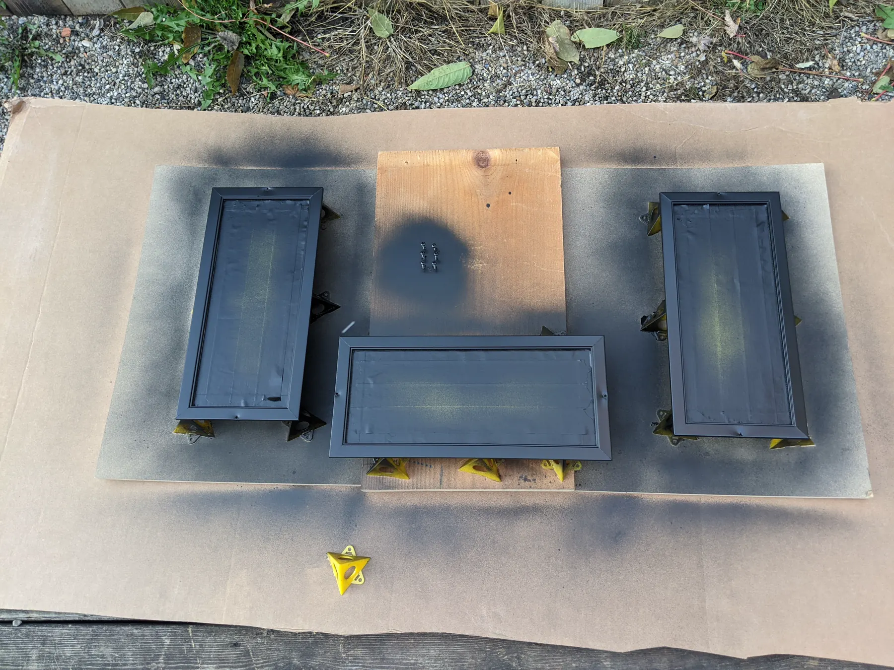 Three vent frames and their screws after receiving an even black finish outdoors.
