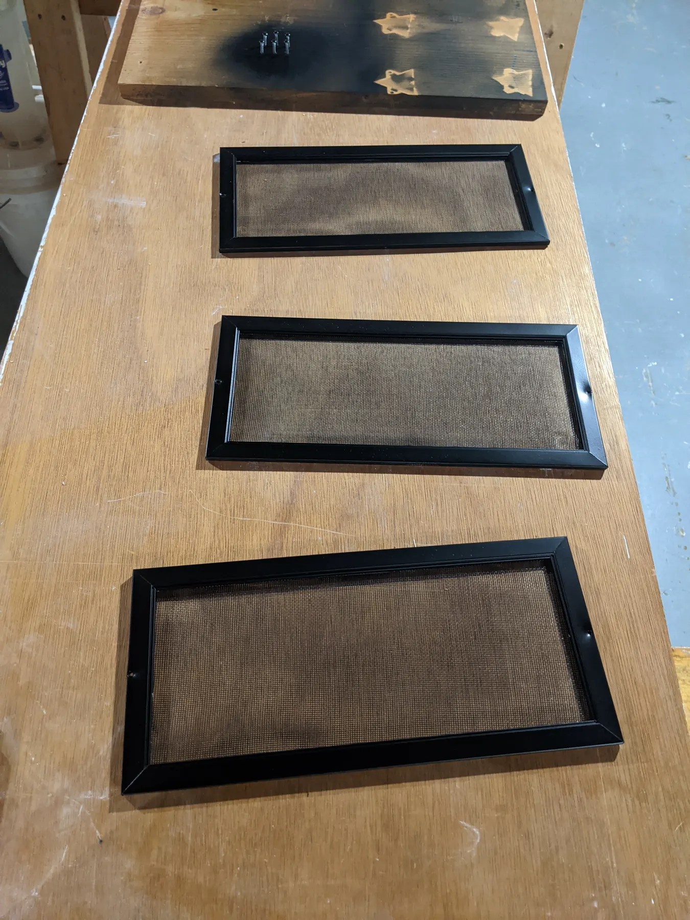 Three finished black screen inserts with the mesh uncovered after painting.