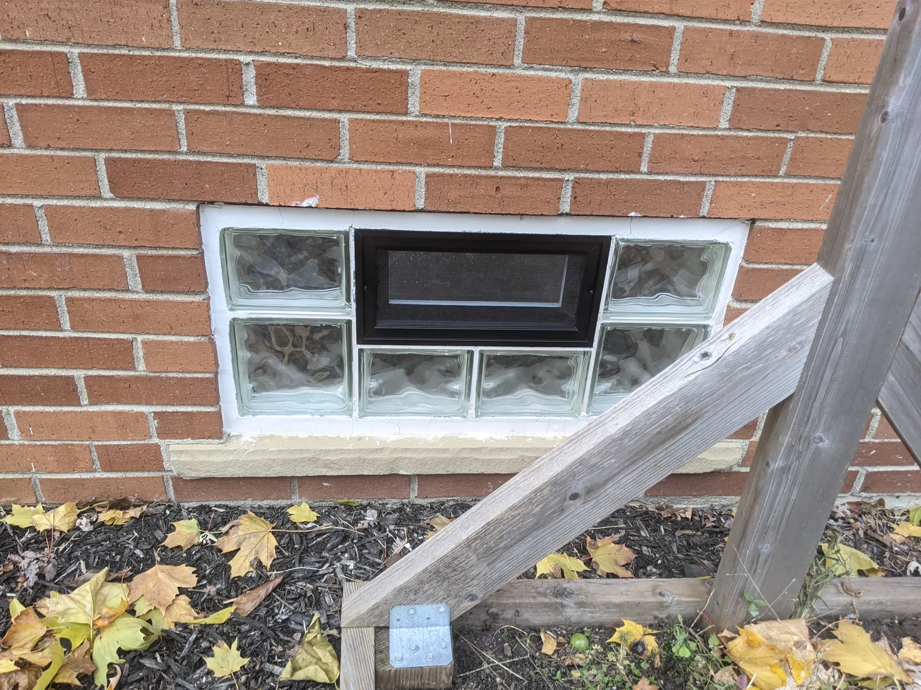 Finished black screen vent reinstalled within a glass-block opening beside the garden stairs.