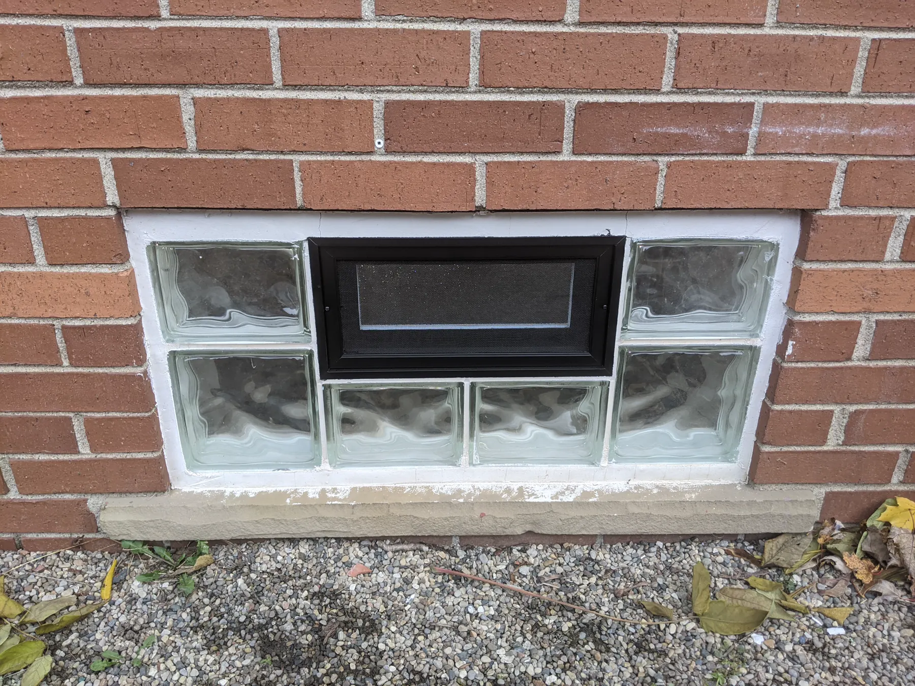 Finished black screen vent centered within a glass-block basement window.