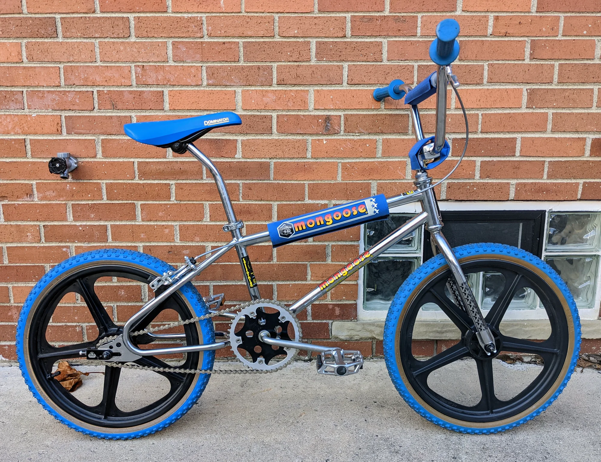 Side profile of a 1985 Mongoose Californian with a bright frame, black five-spoke wheels, and blue tires, saddle, grips, and pads.