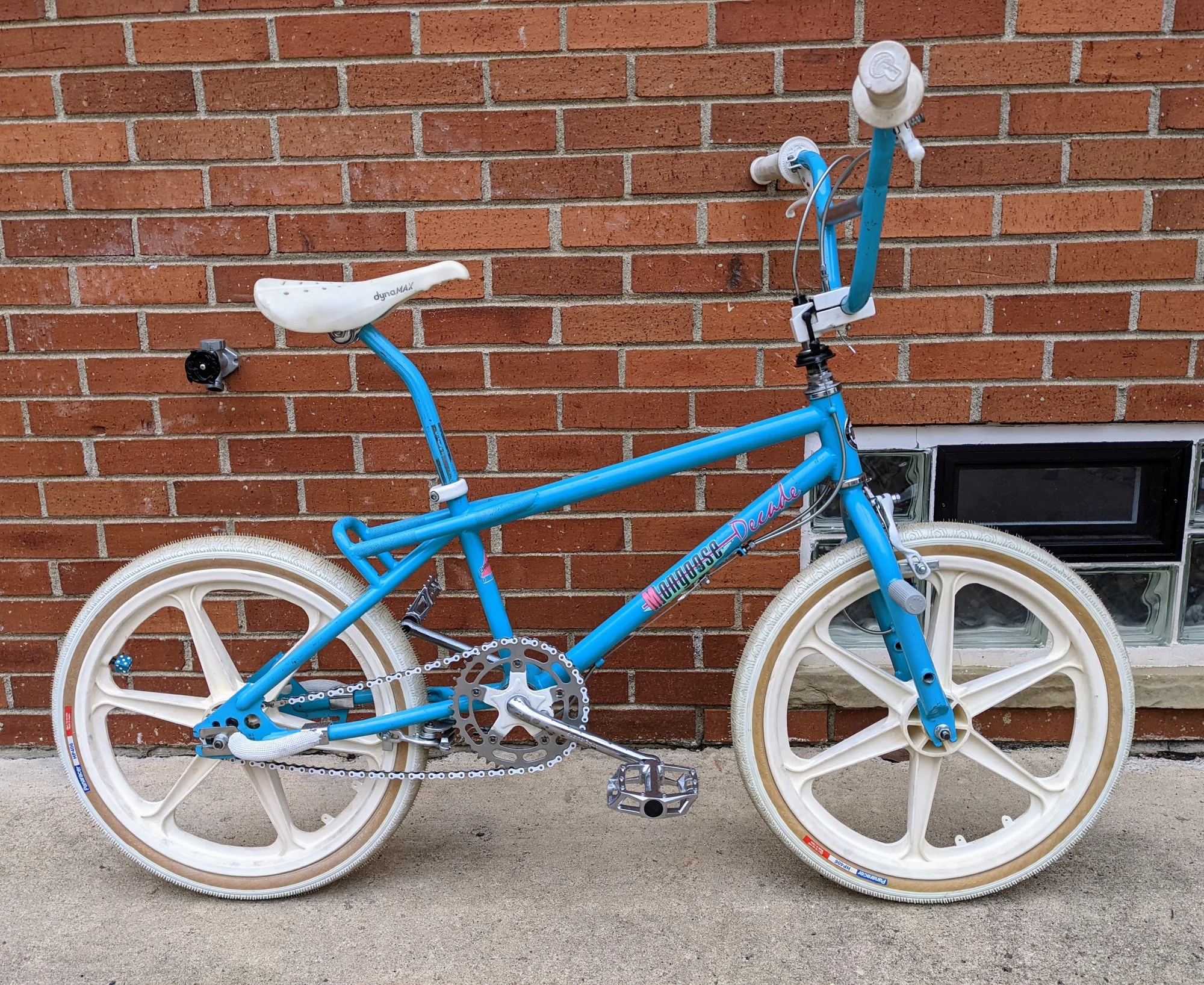 Side profile of a 1987 Mongoose Decade with a light-blue frame and cockpit, plus white five-spoke wheels, tires, saddle, and pads.