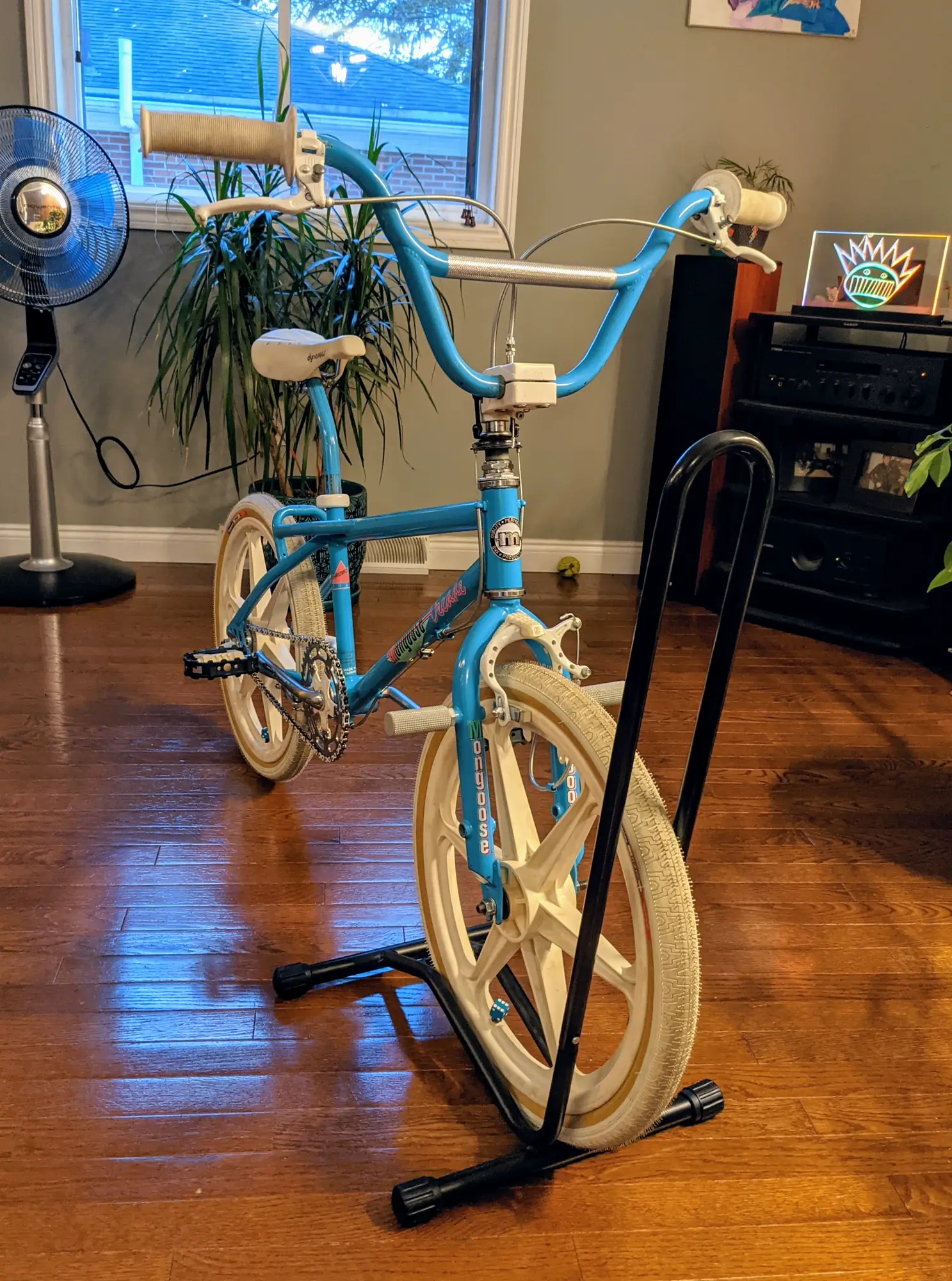 Indoor front-quarter view of the 1987 Mongoose Decade showing the blue cockpit, white controls, frame, and front five-spoke wheel.
