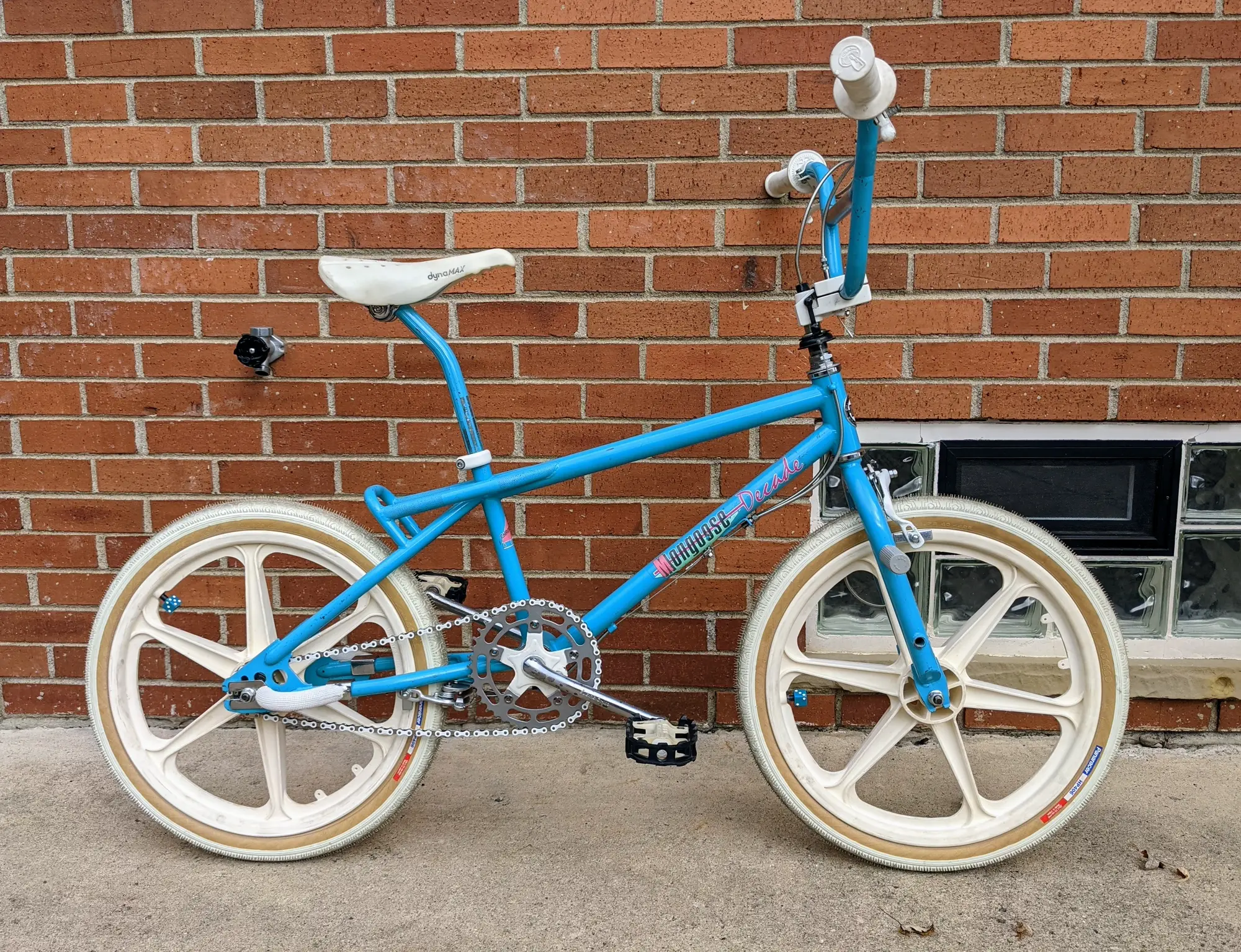 Outdoor side profile of the light-blue 1987 Mongoose Decade with white five-spoke wheels, tires, grips, and saddle.