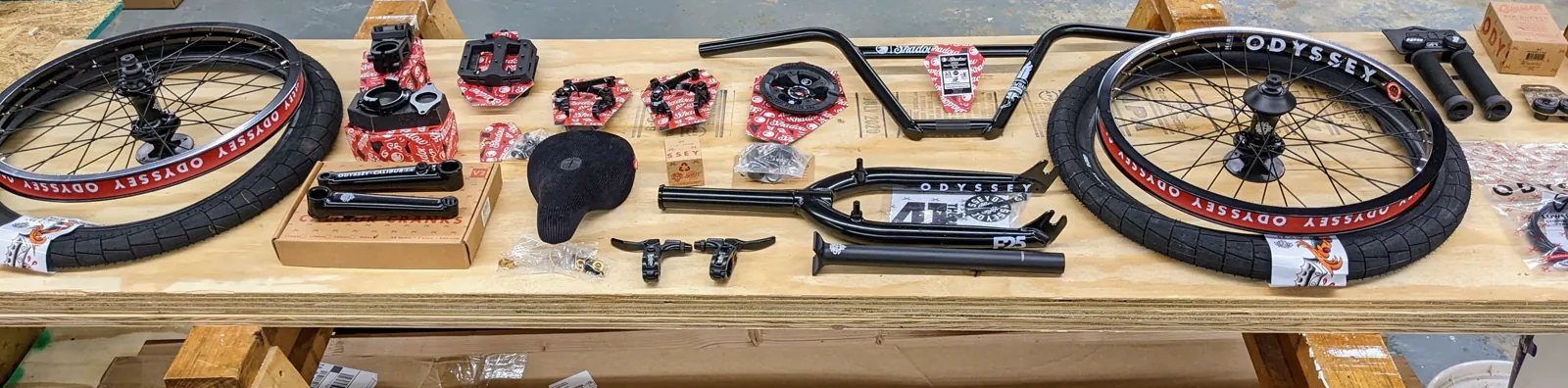 Panoramic bench layout of the Sunday Soundwave build components, including two complete wheels, tires, fork, handlebar, cranks, sprocket, pedals, saddle, grips, and small hardware.