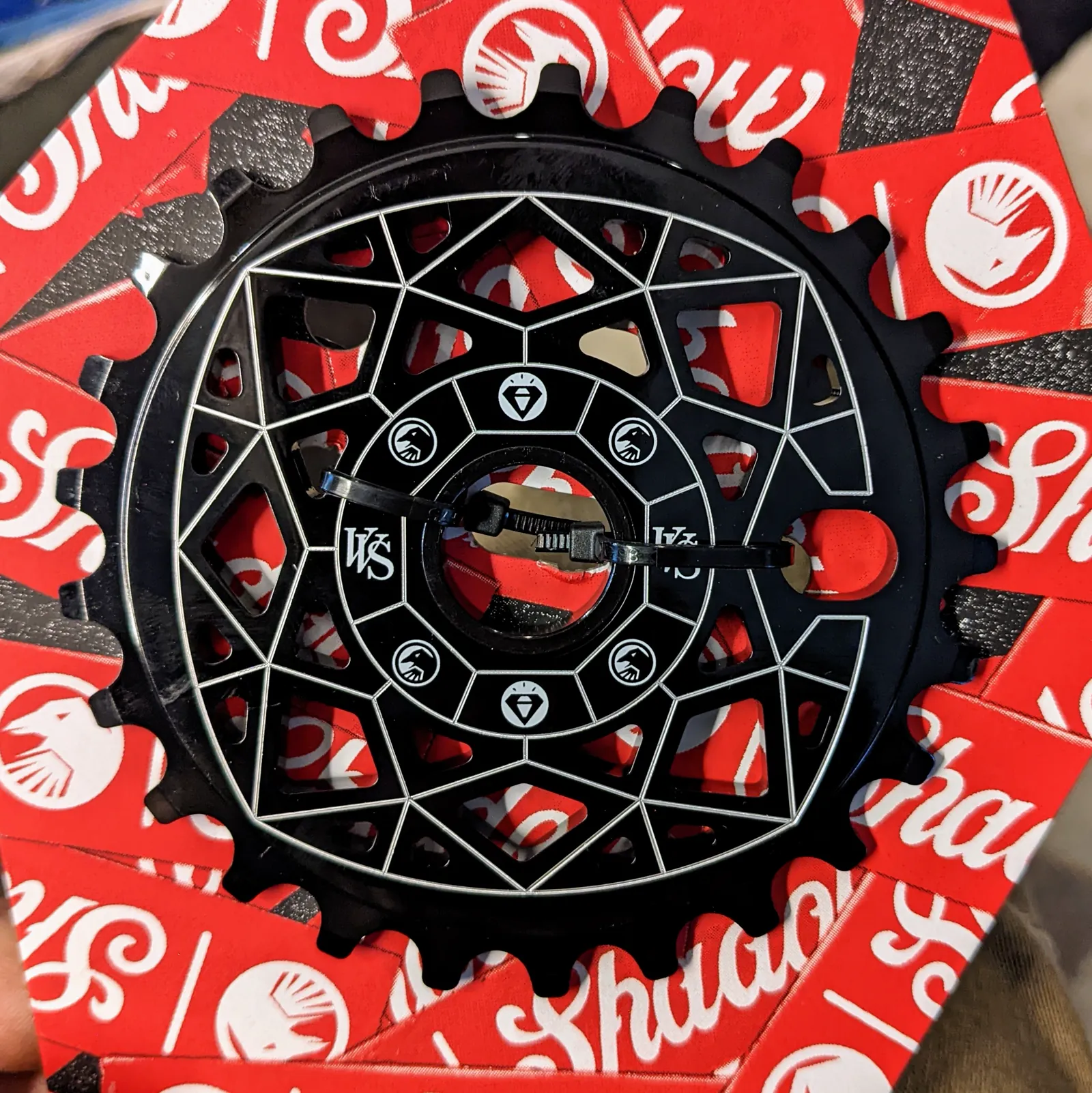 Black patterned BMX sprocket secured in red retail packaging.