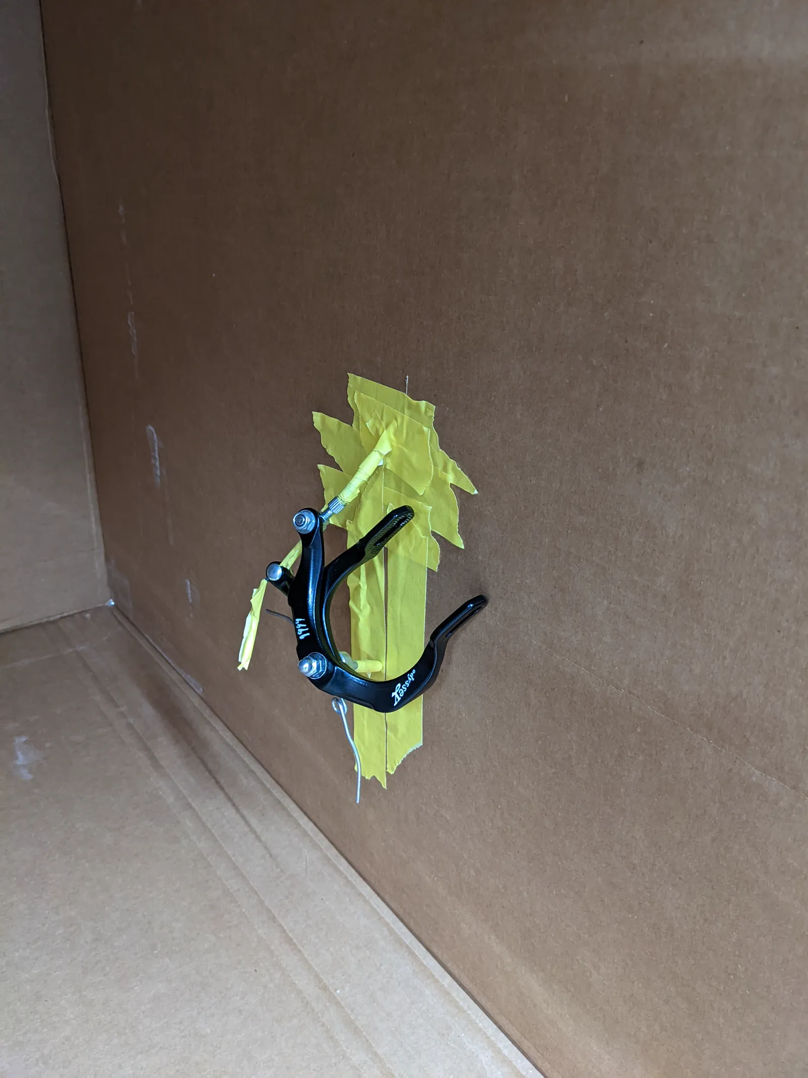 Small part masked with green tape inside a cardboard spray booth.
