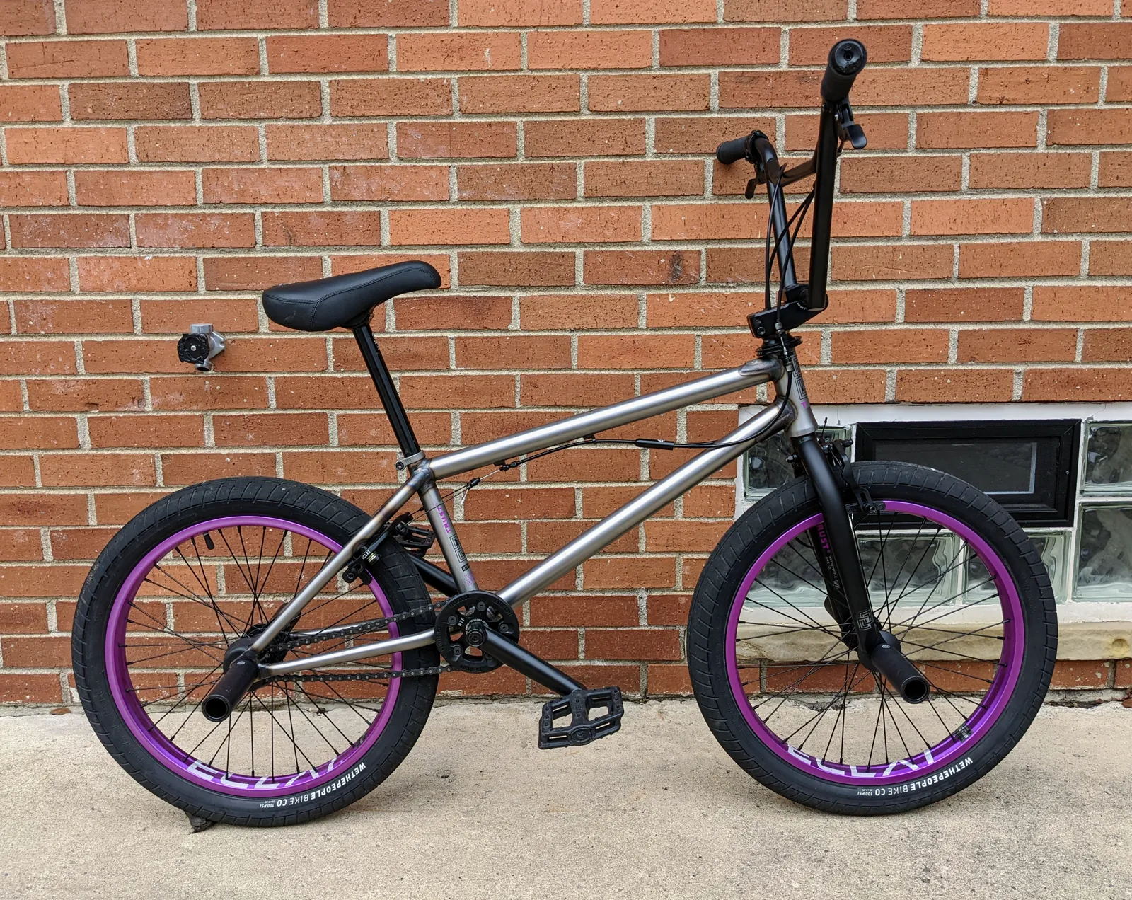 Final side profile of the raw WTP Trust FC with black components and purple rims against a brick wall.
