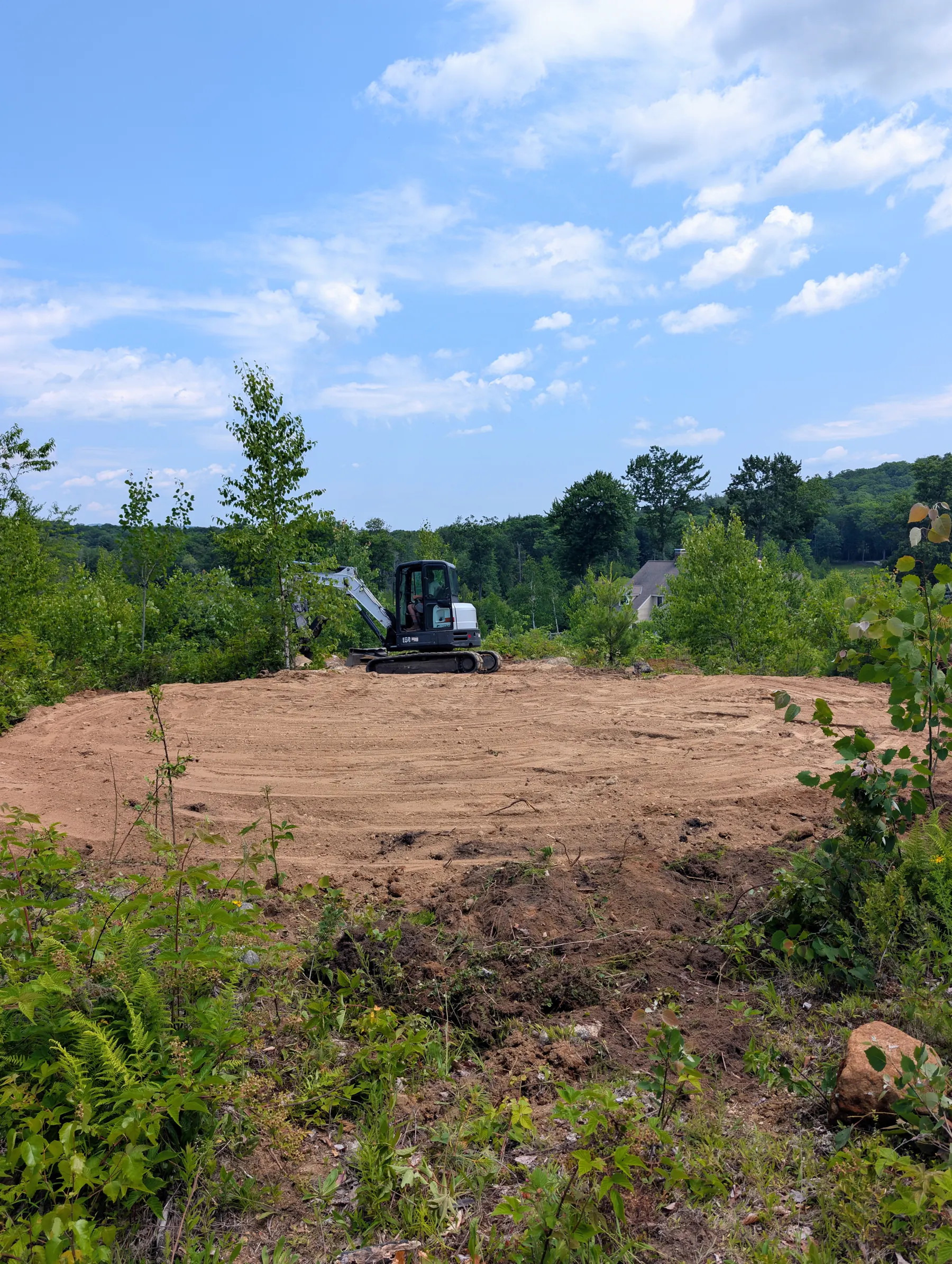 Freshly graded primary campsite with an excavator and a long view over the trees.