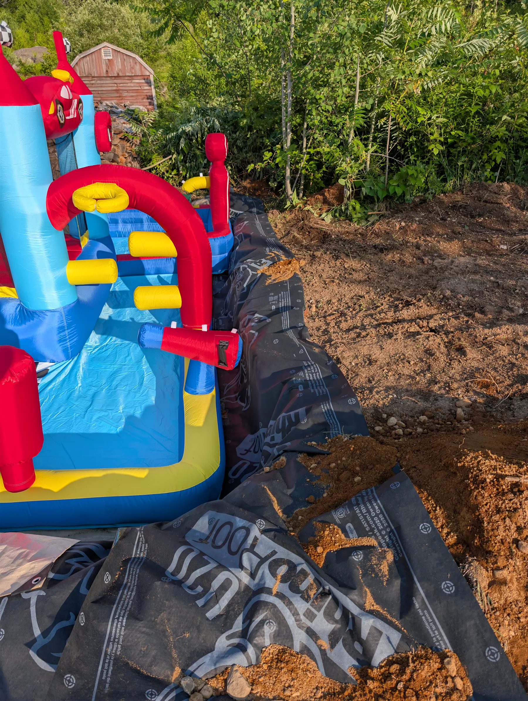 Close view beside the castle showing black underlayment and freshly excavated soil shaping the incoming return-water channel.
