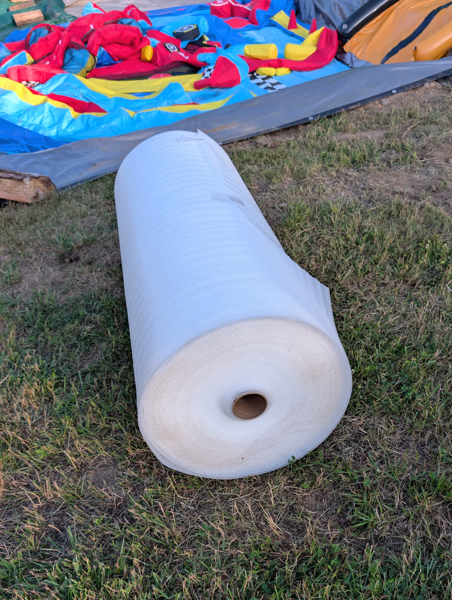 Six-foot-wide roll of white foam beside the deflated water castle before it was trimmed to support the slide-to-basin transition.