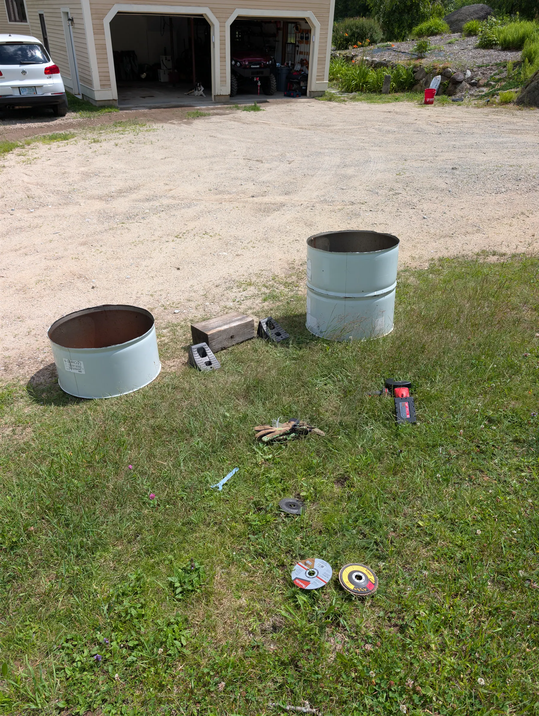 Two cut steel drum sections on the grass with fabrication tools nearby.