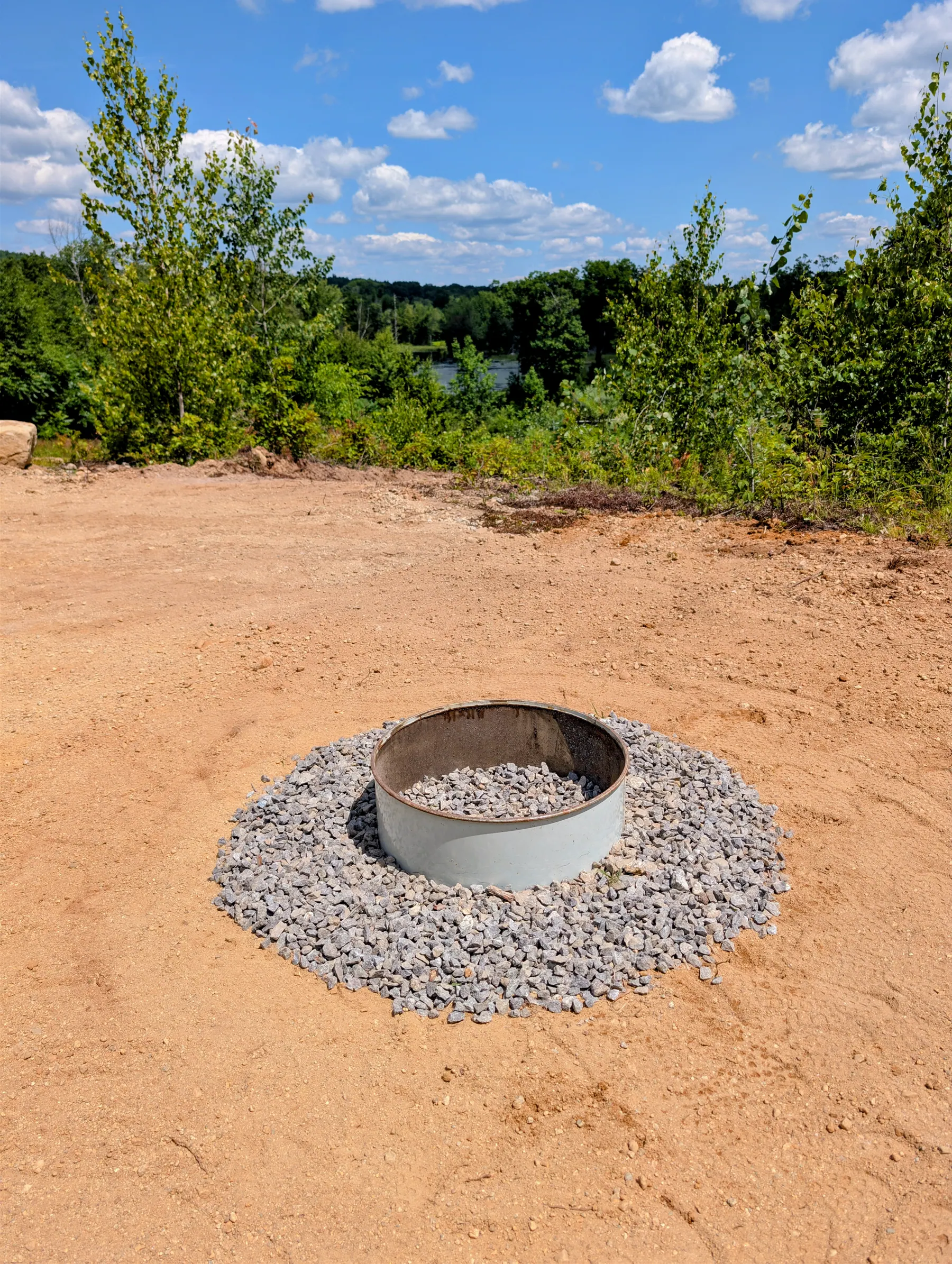 Finished steel fire ring centered within a circular crushed-stone apron on the elevated terrace.