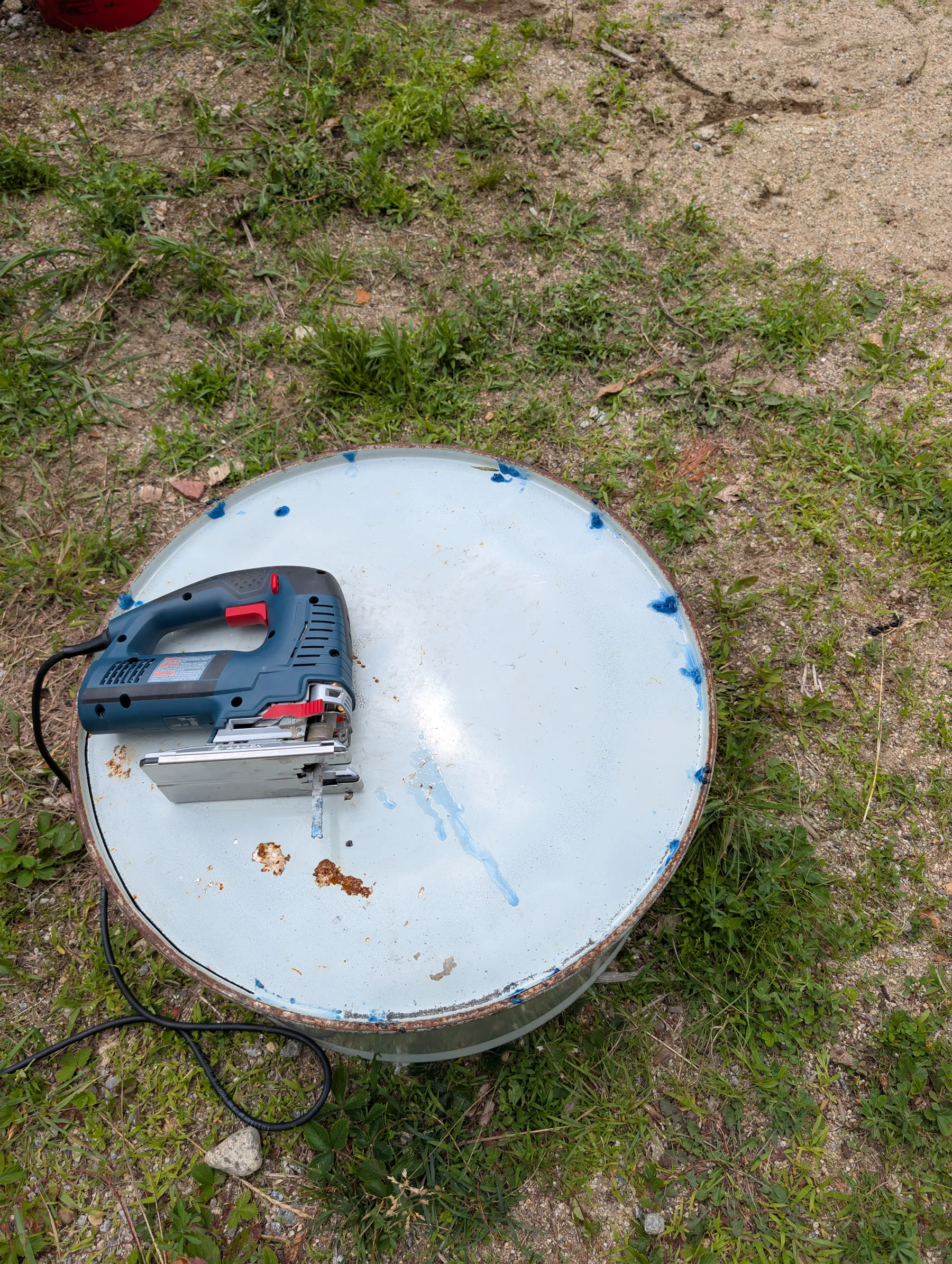Jigsaw resting on the steel drum top during the process of cutting a circle out of the barrel top.