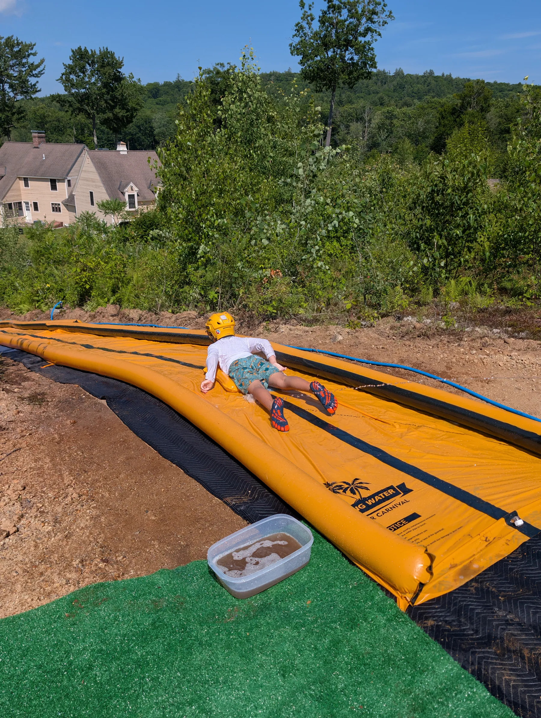 Rider beginning a run from the hilltop launch pad, with artificial turf and a foot-wash basin in the foreground and the house visible below.