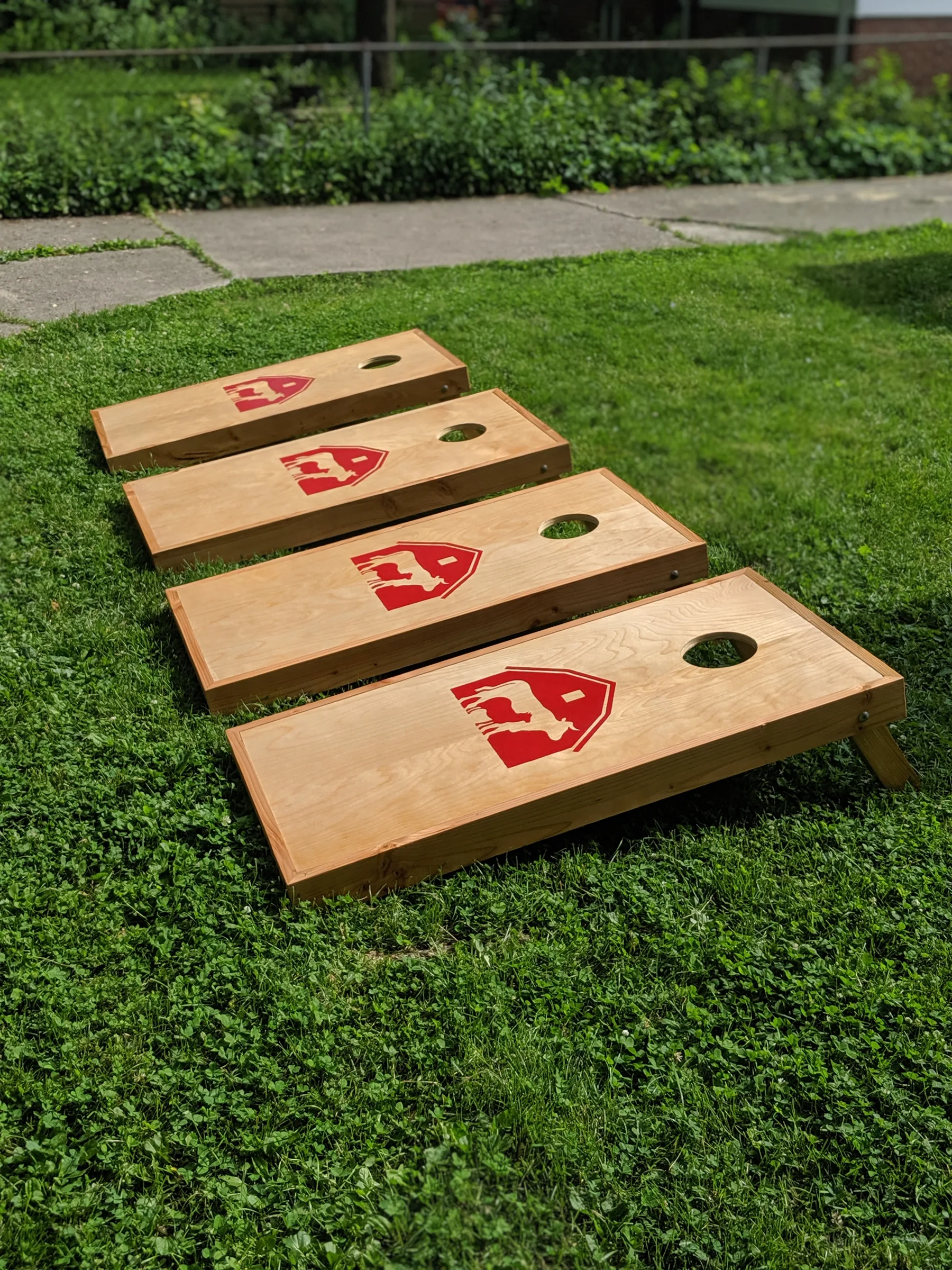 Four completed fir-framed birch cornhole boards arranged as two sets on green grass.