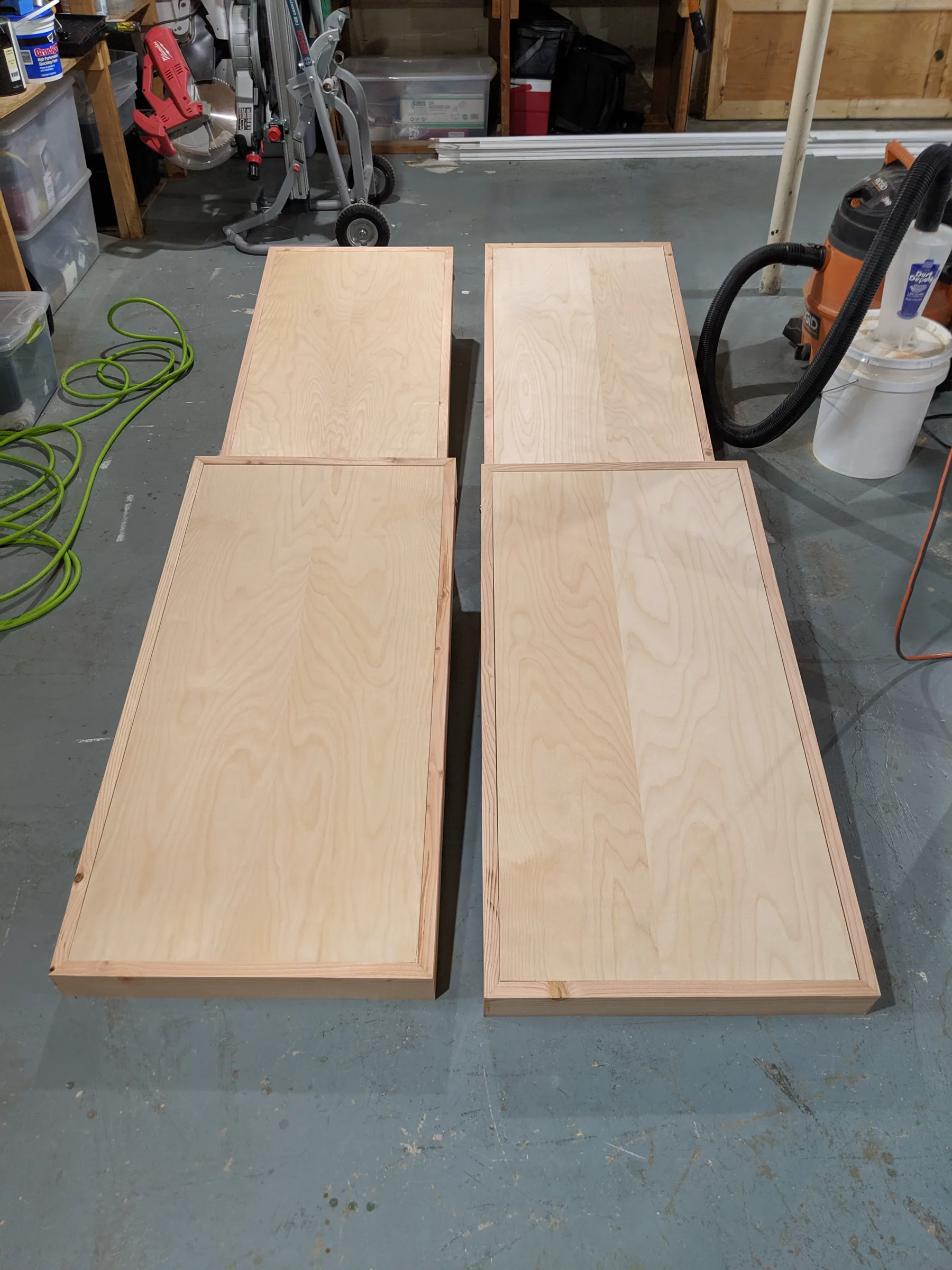 Four unfinished cornhole boards laid out in the workshop, showing birch panels inset within fir perimeter frames.