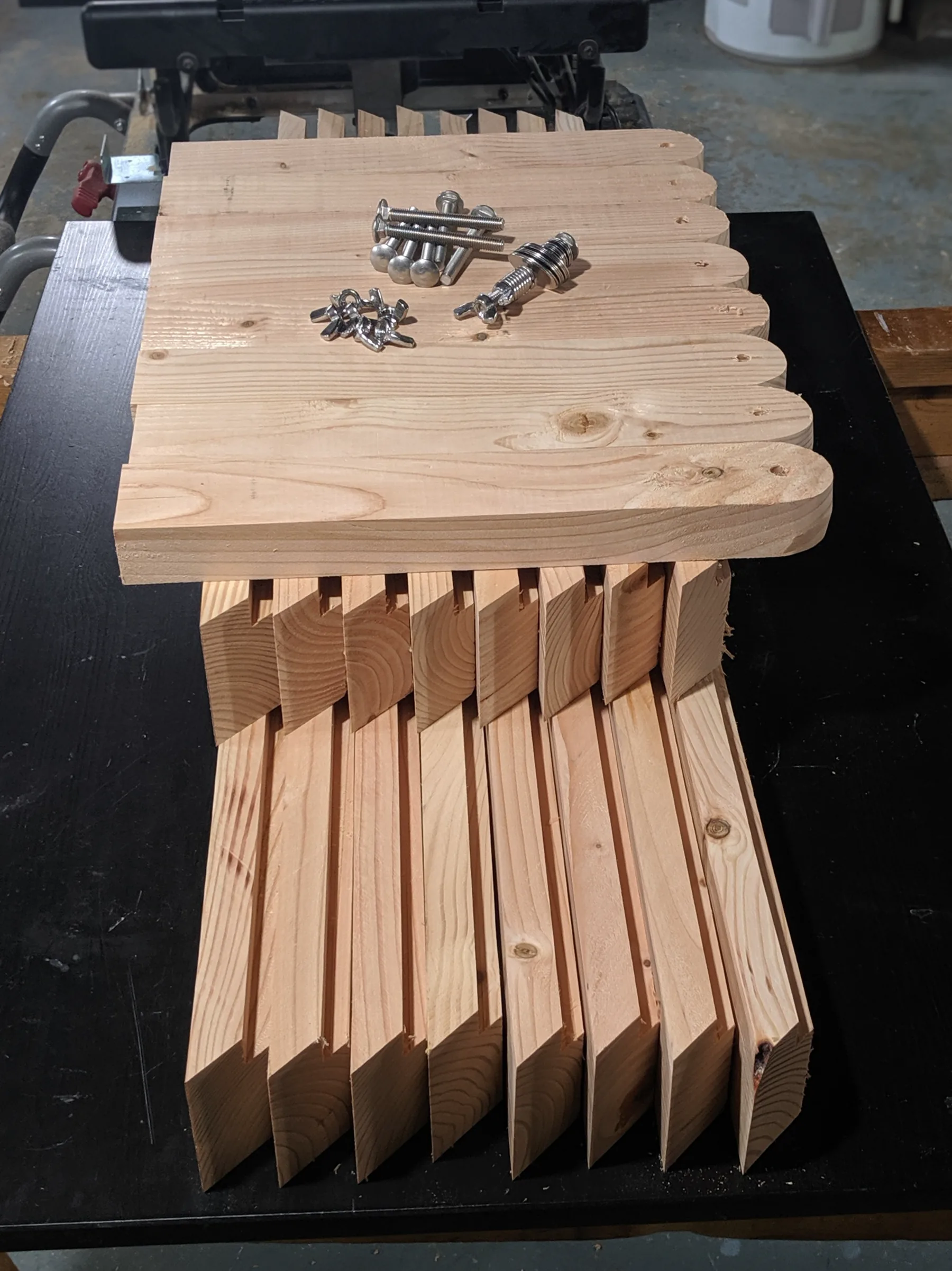 Stacked wooden board components with stainless bolts, washers, and locknuts laid out on top.