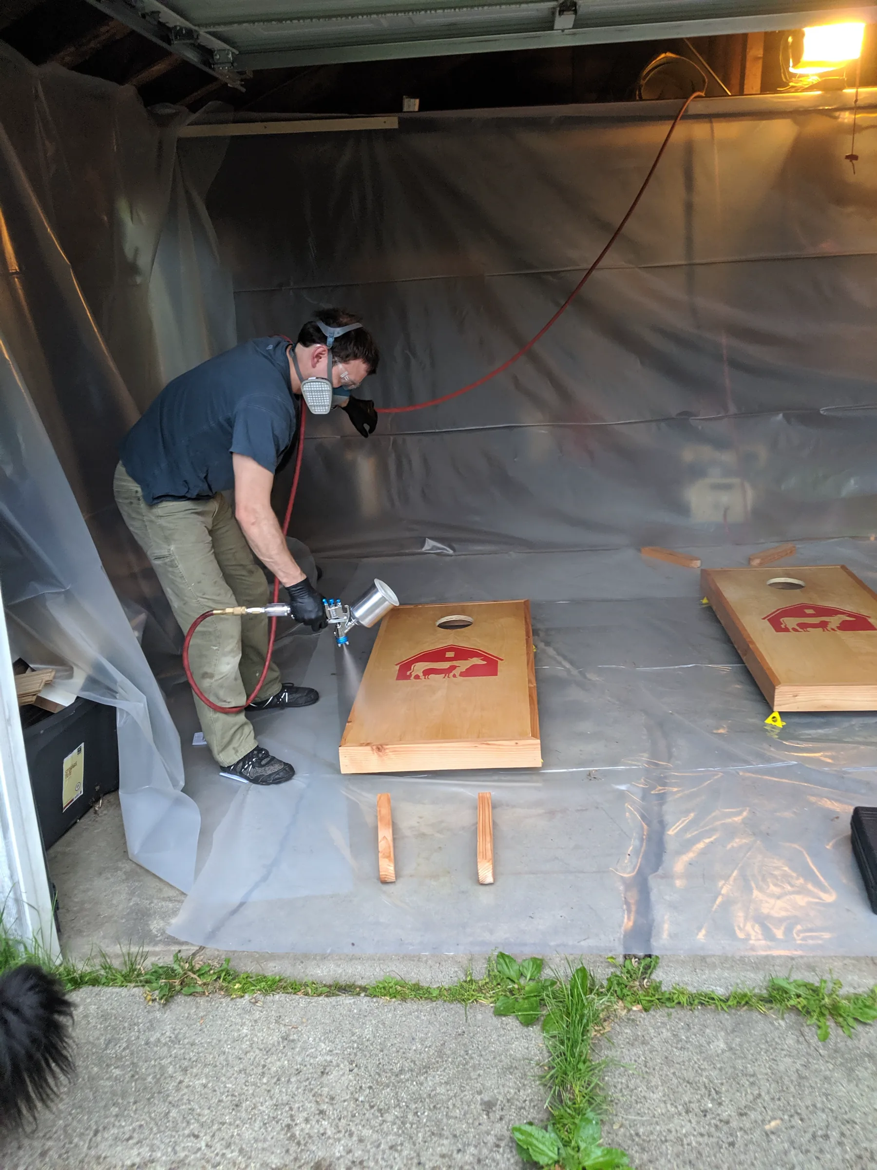 Builder wearing a respirator applying finish to cornhole boards in the finish booth.