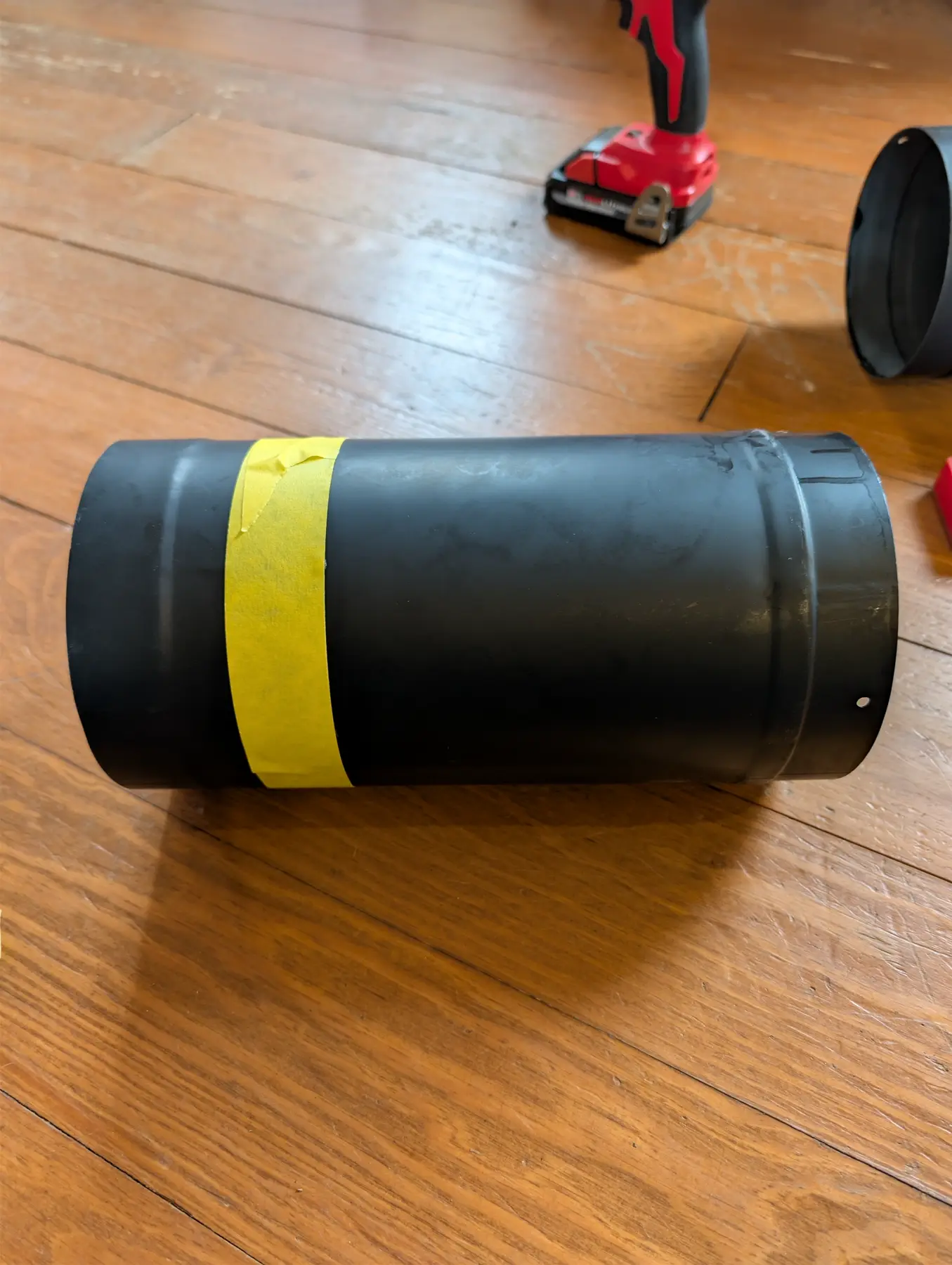 Black round woodstove-pipe adapter section marked with yellow tape.