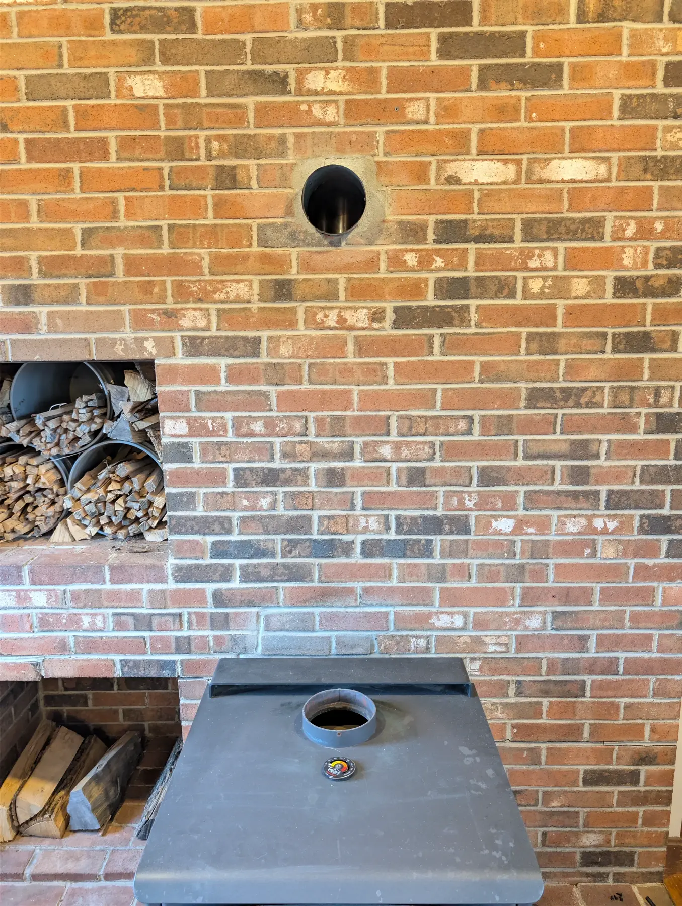 Woodstove positioned below the round chimney thimble in the brick wall for route alignment.