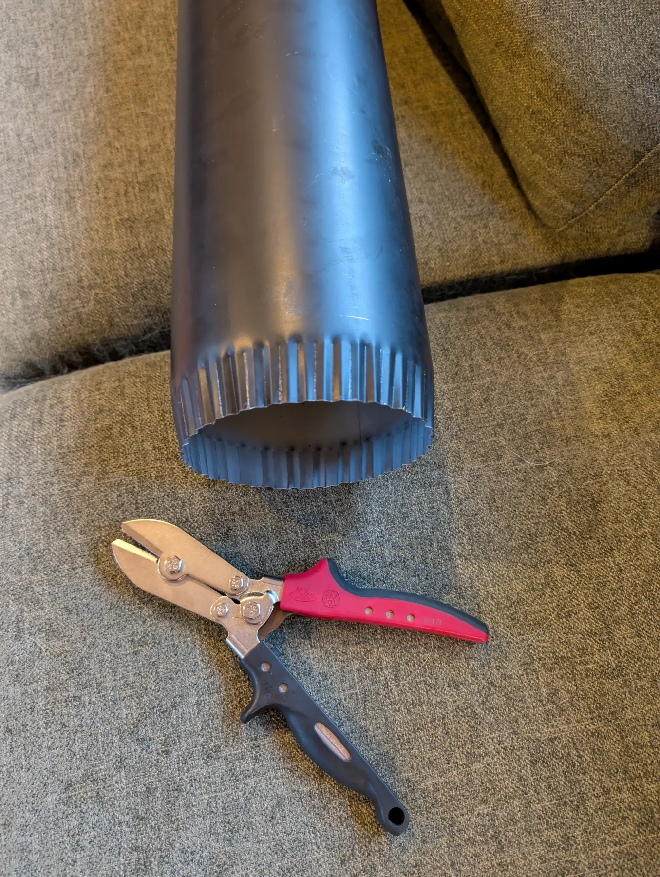 Hand crimper being used to form the end of a black woodstove connector pipe.