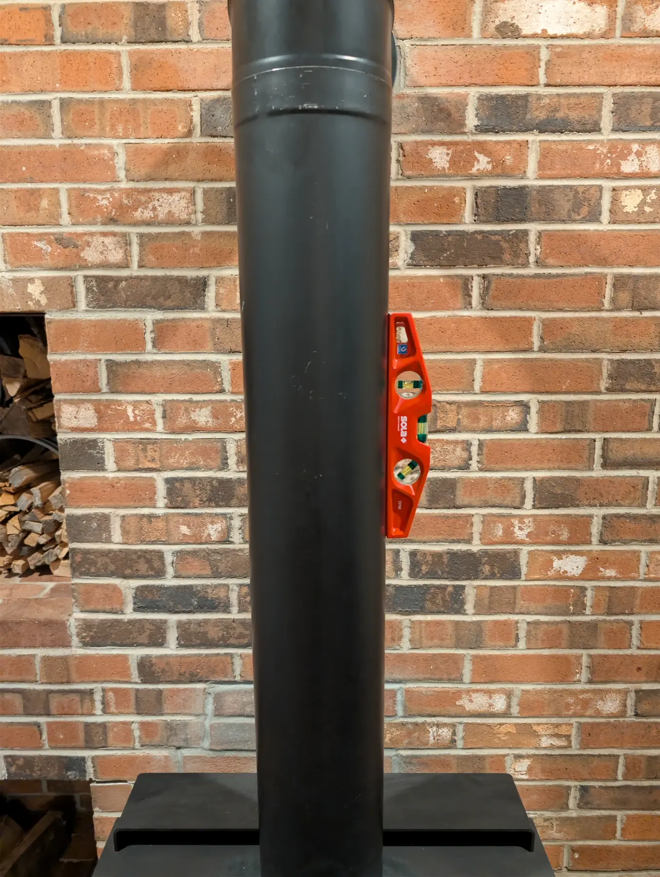 Magnetic level attached to the vertical black stove-pipe run against the brick wall.