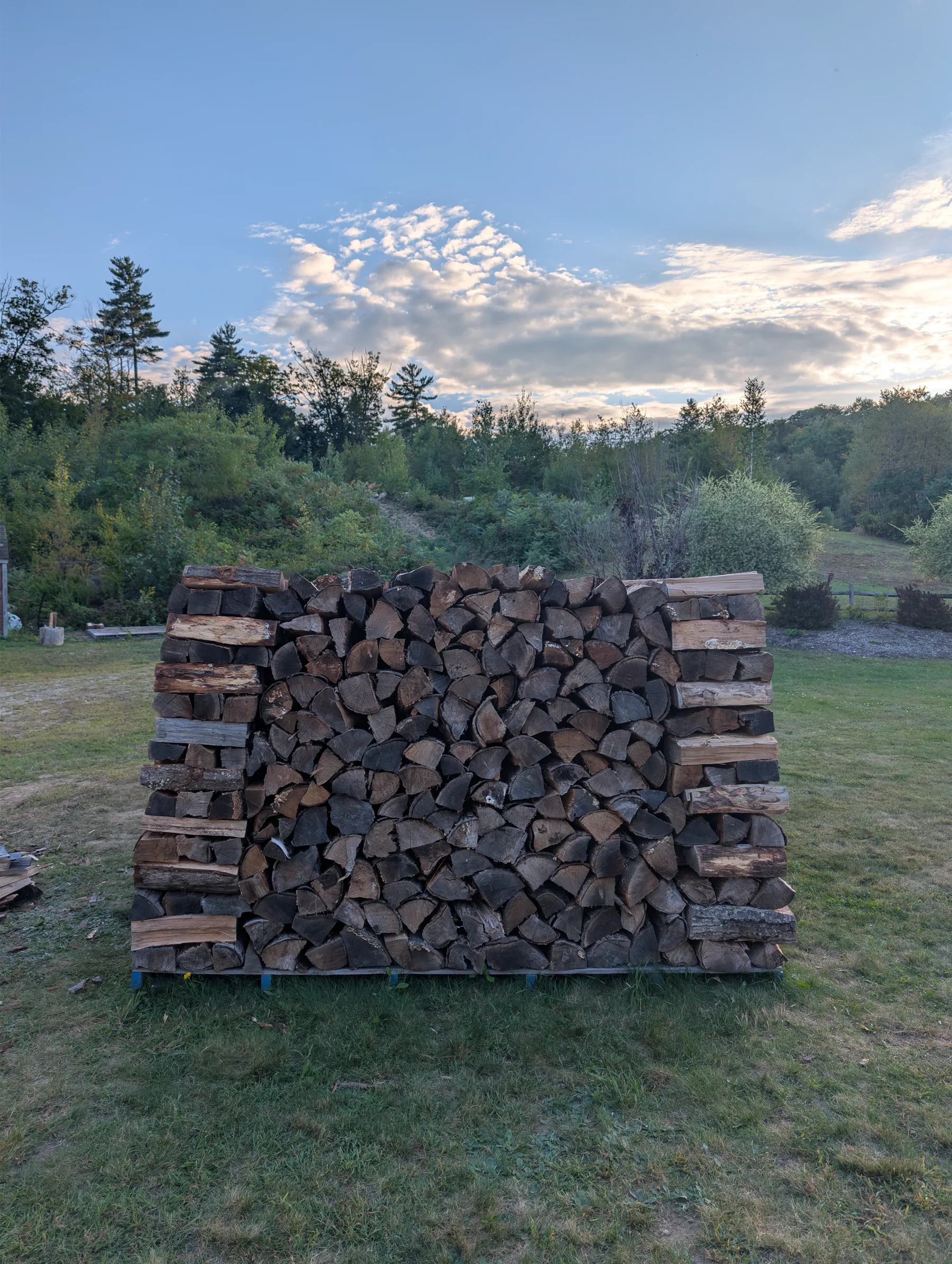 End view of the firewood stack showing corner towers and a dense wall that narrows inward toward the top.