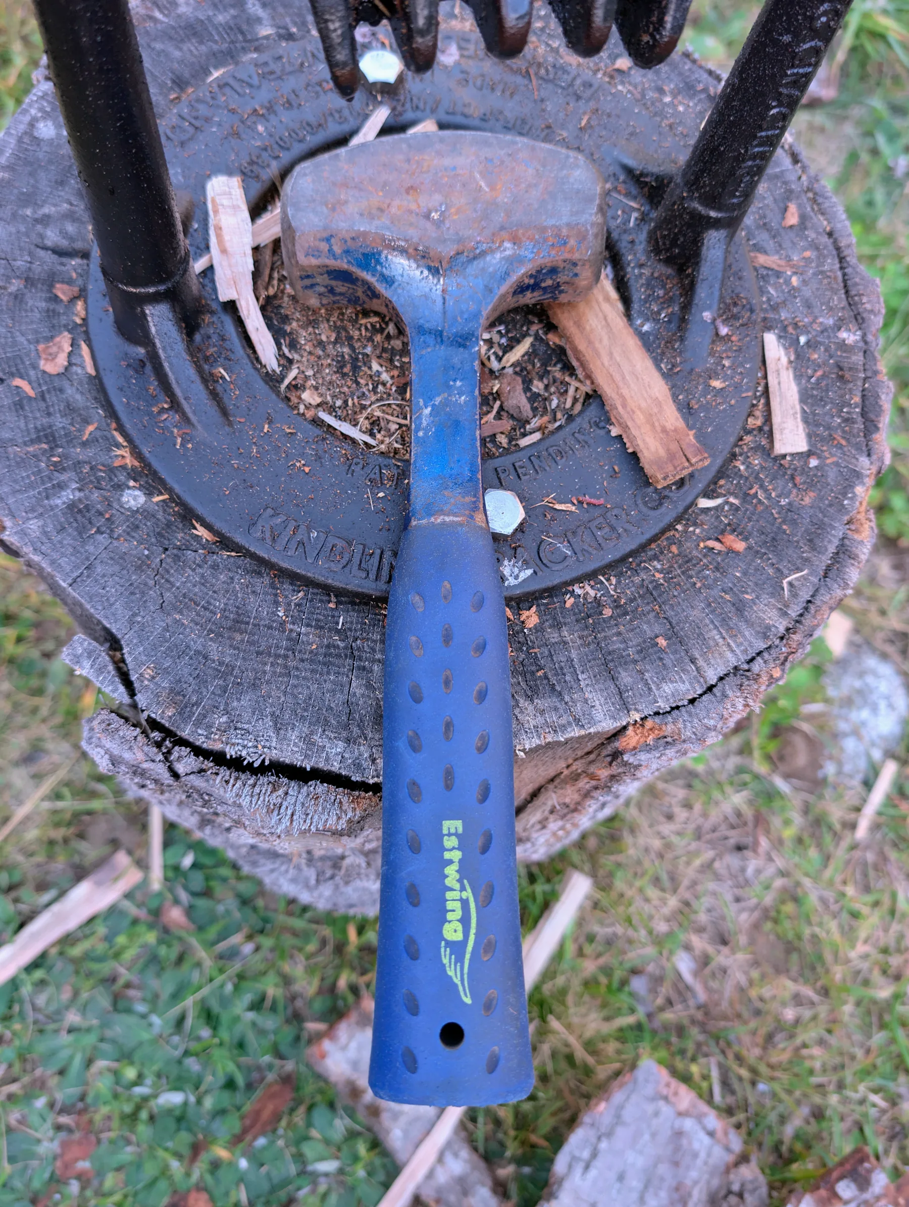 Blue-handled three-pound masonry hammer resting on a stump beside the firewood stack.