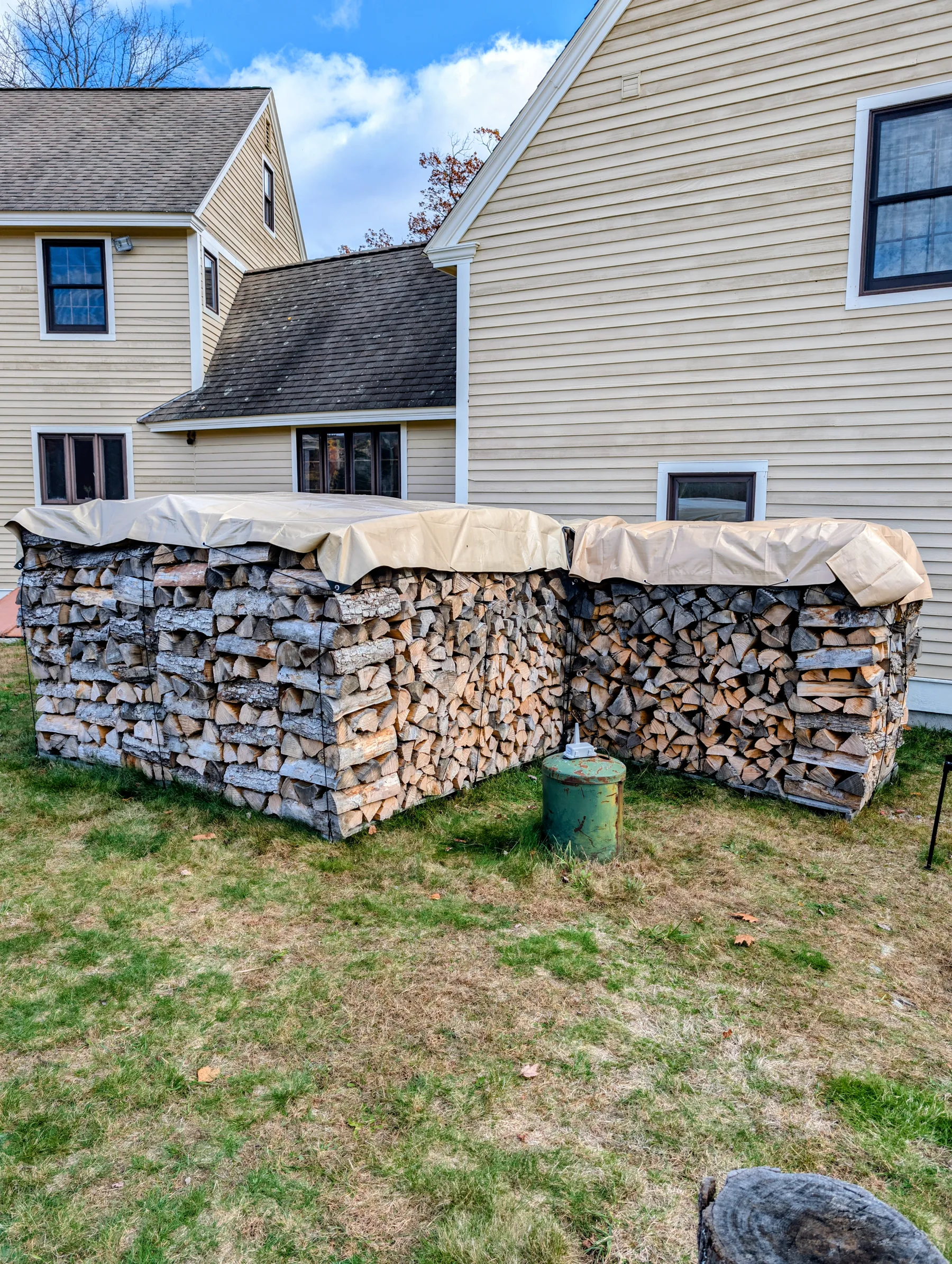 Wide final view of several rectangular firewood stacks covered by fitted tan tarps and restrained around their sides.