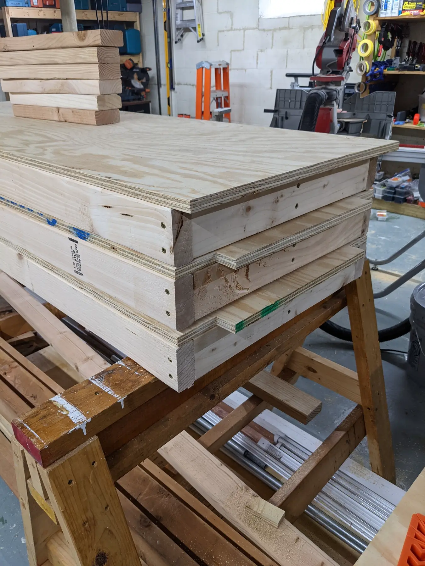 Cut lumber and shelf boards stacked at the workbench for the first basement supply shelf.