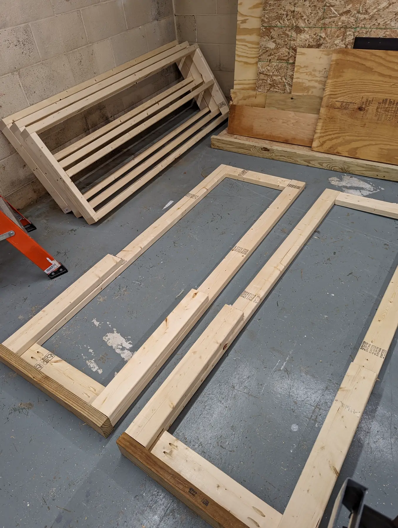 Workshop shelf frame sides with pressure-treated feet and long rails laid out on the basement floor.